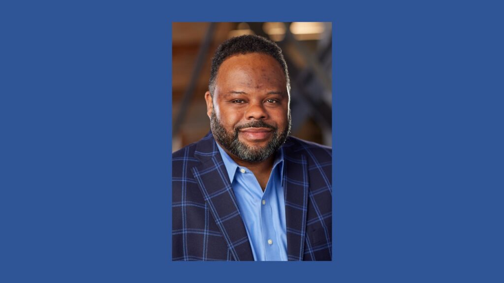 This is a photo of Gerard Hollins, Jr. He is joining STL to temporarily oversee STL's Finance and Accounting Team. The photo is a portrait shot of Mr. Hollins dressed in a dark checked suit with light blue stripes, He is wearing an open collared light blue shirt.