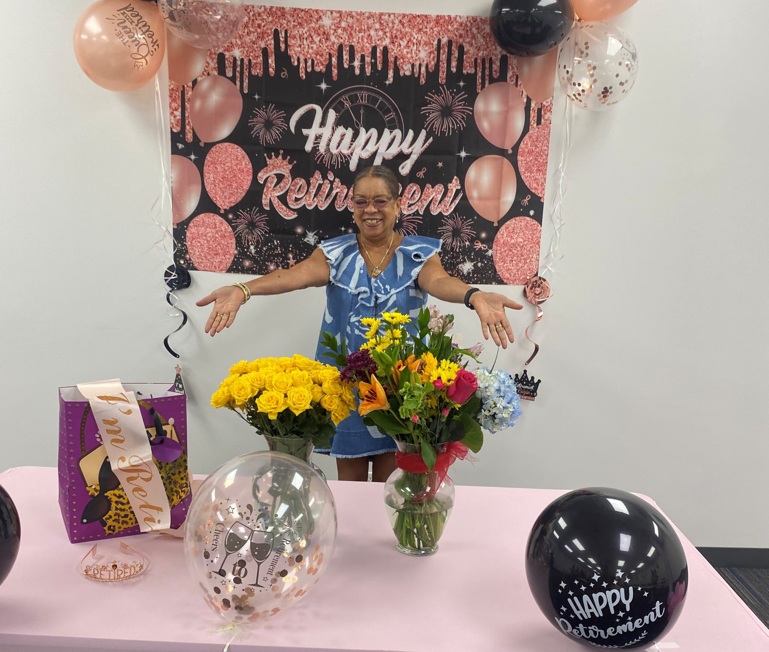 This photo shows Barbara Carter in front of a banner announcing her retirement from STL and a table with gifts and flowers at her retirement party at the end of August in 2026,