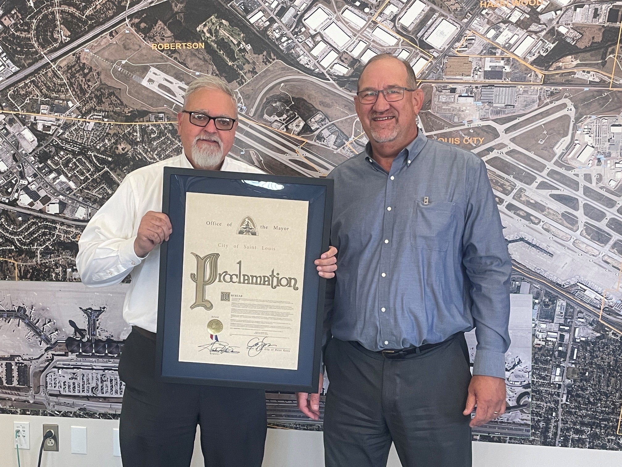 This is a photo from Reed Glasener's retirement party. Reed, on the left of the photo, was presented with a mayoral proclamation by Jerry Beckman, on the right. Beckmann is the airport's acting director. In the photo, Reed is holding the framed proclamation.